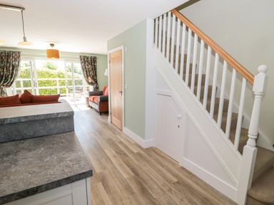 An open living area with a staircase, wooden floor, stone countertops, sofas, and sliding glass doors at Rose Lodge in High Newton-by-the-Sea near Embleton