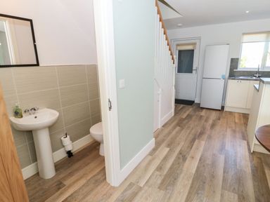 A hallway with a half bathroom on the left and a kitchen area with a refrigerator and sink at Rose Lodge in High Newton-by-the-Sea near Embleton