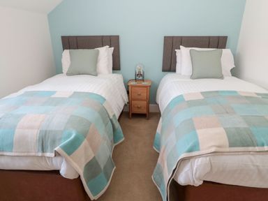 A bedroom with two single beds with grey headboards and a wooden nightstand in between at Rose Lodge in High Newton-by-the-Sea near Embleton
