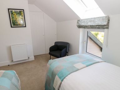 A bedroom with two beds a window a black armchair a radiator and a framed picture at Rose Lodge in High Newton-by-the-Sea near Embleton