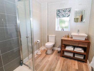 A bathroom with a glass shower, toilet, wooden vanity with a sink and towels at Rose Lodge High Newton-by-the-Sea near Embleton