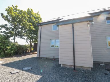 Exterior view of a house with gravel ground and trees at Rose Lodge in High Newton-by-the-Sea near Embleton