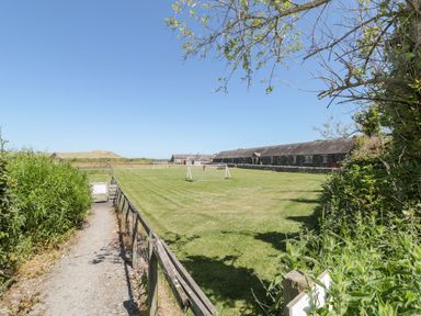 A grassy field with soccer goals next to a long stone building and a path with a wooden fence at Rose Lodge in High Newton-by-the-Sea near Embleton