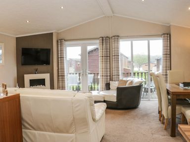 A living room with sofas a wall mounted television a dining table and chairs and large windows with curtains at Walkers Rest in Warton near Carnforth