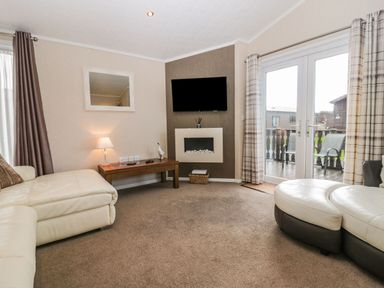 A living room with cream sofas wooden coffee table wall mounted television and glass doors leading outside at Walkers Rest in Warton near Carnforth