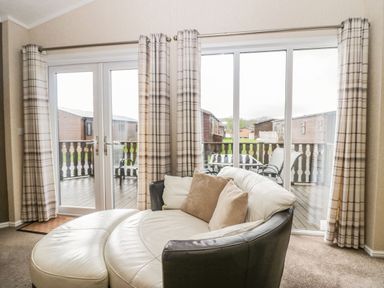 A living room with a round white sofa and plaid curtains in front of sliding glass doors at Walkers Rest in Warton near Carnforth