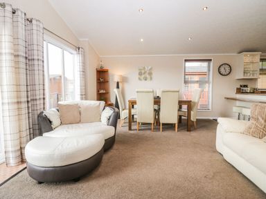 A living room with sofa, cushions, dining table with chairs, corner shelf, lamp, and windows at Walkers Rest in Warton near Carnforth