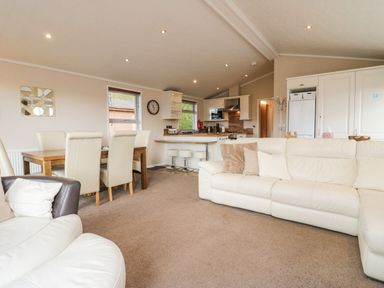 An open plan living area with a white sofa dining table with chairs and kitchen in the background at Walkers Rest in Warton near Carnforth
