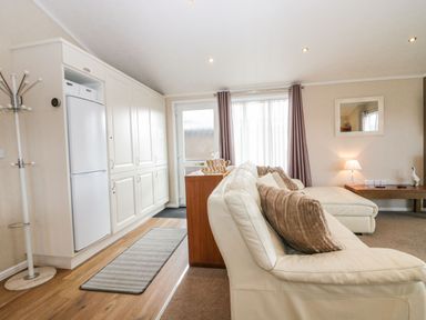 A living room with a white couch and brown cushions near a wooden table with a lamp and mirror at Walkers Rest in Warton near Carnforth