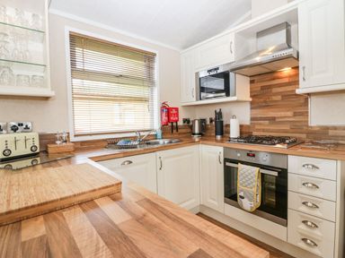 A kitchen with white cabinets a gas stove an oven a microwave a toaster and a window with blinds at Walkers Rest in Warton near Carnforth