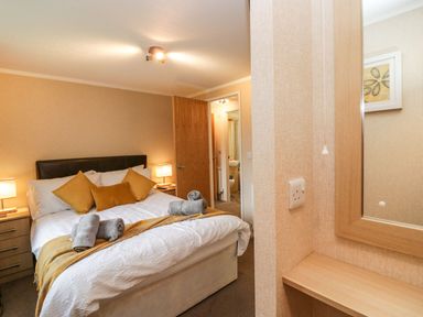 A bedroom with a double bed with rolled towels and cushions bedside tables with lamps and an open door leading to a bathroom at Walkers Rest in Warton near Carnforth