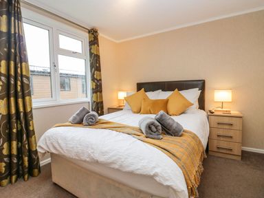 A bedroom with a double bed pillows and rolled towels next to a window with patterned curtains at Walkers Rest in Warton near Carnforth