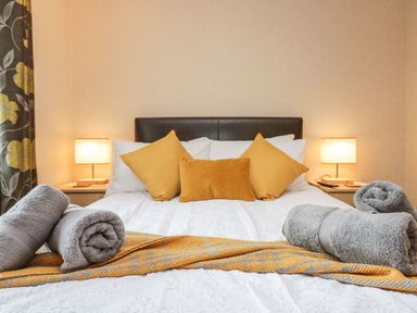 A bedroom with a double bed with yellow pillows and gray rolled towels on a blanket at Walkers Rest in Warton near Carnforth
