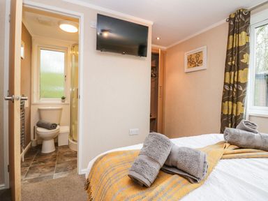 A bedroom with folded towels on the bed a wall-mounted television an open door to a bathroom and a window with curtains at Walkers Rest in Warton near Carnforth