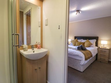 A bedroom with a bed and bedside tables with lamps visible through a doorway from a bathroom with a sink and mirror at Walkers Rest in Warton near Carnforth