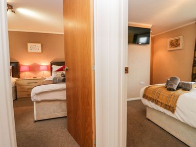 Two bedrooms with beds and bedside tables separated by a partially open wooden door at Walkers Rest in Warton near Carnforth