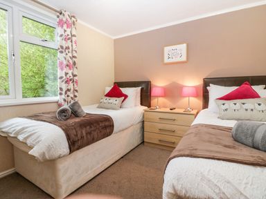 A bedroom with two single beds a nightstand with two lamps and a window with floral curtains at Walkers Rest in Warton near Carnforth