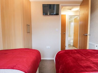 A bedroom with two single beds covered with red blankets a wooden wardrobe and a wall-mounted television at Walkers Rest in Warton near Carnforth