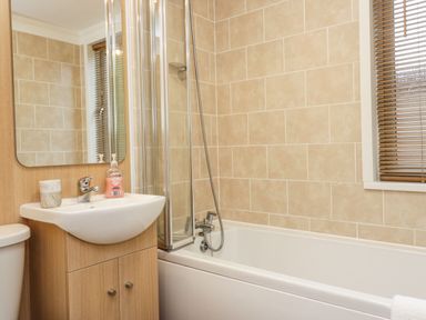 A bathroom with a sink cabinet mirror bathtub shower screen and window blinds at Walkers Rest in Warton near Carnforth