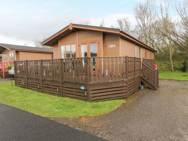 A wooden lodge with a fenced deck and a gravel driveway at Walkers Rest in Warton near Carnforth