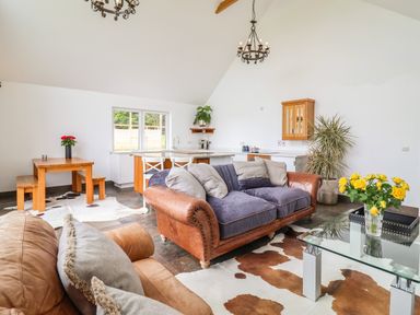 A living room with leather sofas, a glass coffee table with yellow flowers, and a dining area with wooden table and benches at Polly's Annexe in Levington
