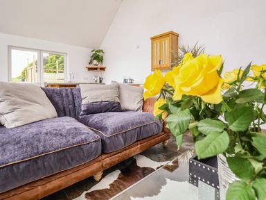 A living room with a purple and brown sofa yellow flowers on a glass table and kitchen in the background at Pollys Annexe in Levington