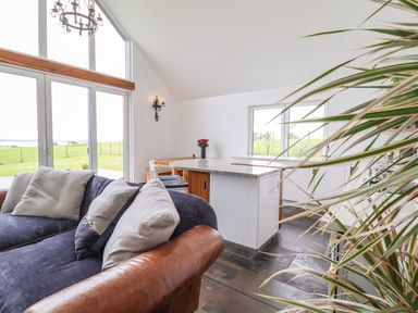 A living room with a sofa and pillows next to a kitchen island and windows overlooking a grassy field at Polly's Annexe in Levington