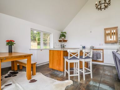 A kitchen and dining area with wooden table and bench a kitchen island with two chairs and a cowhide rug at Polly's Annexe in Levington