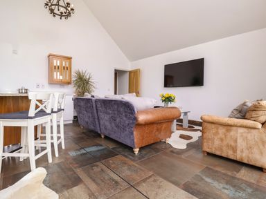 A living room with sofas a wall mounted television and a countertop with stools at Polly's Annexe in Levington