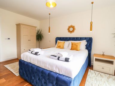 A bedroom with a blue upholstered bed white linens yellow pillows wooden nightstands and a beige wardrobe at Pollys Annexe in Levington