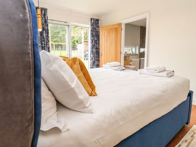 A bedroom with a large bed with white sheets and pillows with a door leading to a bathroom and sliding glass doors with curtains at Polly's Annexe in Levington