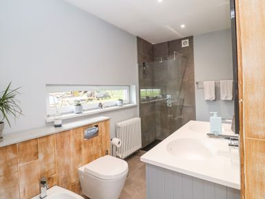 A bathroom with a double sink vanity a toilet a bidet a walk-in shower and a window with potted plants at Polly's Annexe in Levington