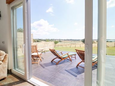 A patio with wooden chairs and loungers looking out over a grassy field at Polly's Annexe in Levington