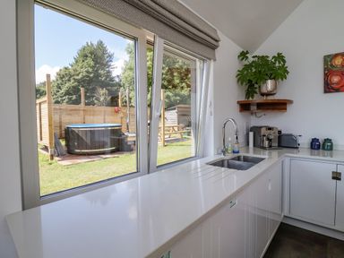 A kitchen with a sink coffee machine and potted plant next to a large window showing a hot tub and picnic table outside at Pollys Annexe in Levington