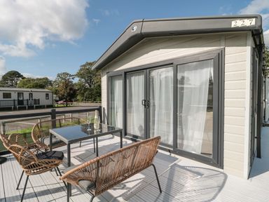 A patio with a table and chairs outside a mobile home with sliding glass doors at The Olive Lodge 227 Sycamore in New Milton