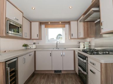 A kitchen with built-in microwave oven wine cooler gas stove oven sink toaster kettle and wooden cabinets at The Olive Lodge 227 Sycamore in New Milton