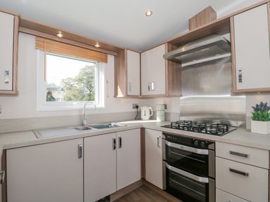 A kitchen with a sink below a window a gas stove oven and cabinets at The Olive Lodge 227 Sycamore in New Milton