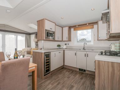 A kitchen with wooden cabinets and a dining table with chairs and wine glasses at The Olive Lodge 227 Sycamore in New Milton
