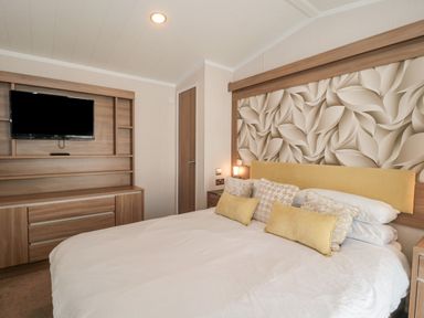 A bedroom with a bed with pillows and a wall-mounted TV at The Olive Lodge 227 Sycamore in New Milton