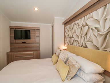 A bedroom with a bed featuring yellow and beige pillows and a wooden cabinet with a mounted TV at The Olive Lodge 227 Sycamore in New Milton
