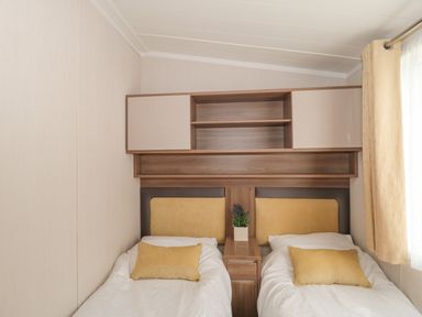 A bedroom with two single beds separated by a wooden nightstand with a plant and shelves above at The Olive Lodge 227 Sycamore in New Milton