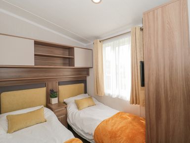 A bedroom with two single beds a window with curtains and overhead storage at The Olive Lodge 227 Sycamore in New Milton
