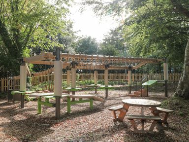 An outdoor playground with climbing equipment and a round picnic table with benches at The Olive Lodge 227 Sycamore in New Milton