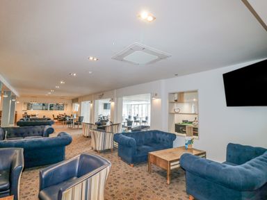 A seating area with blue and striped armchairs and wooden tables in a cafe at The Olive Lodge 227 Sycamore in New Milton