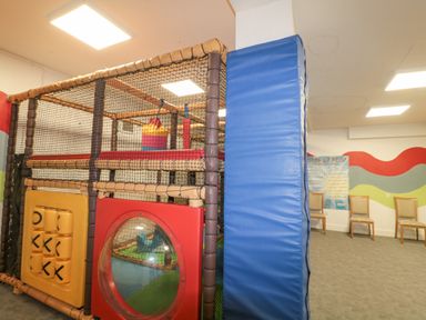 An indoor play area with a padded climbing structure and chairs against a wall with colorful wavy patterns at The Olive Lodge 227 Sycamore in New Milton