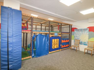 An indoor play area with padded climbing structures netting tic tac toe game and two chairs with rules of play sign on the wall at The Olive Lodge 227 Sycamore in New Milton