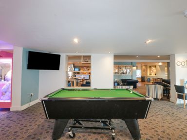 A room with a pool table a television mounted on the wall striped chairs and a cafe sign at The Olive Lodge 227 Sycamore in New Milton
