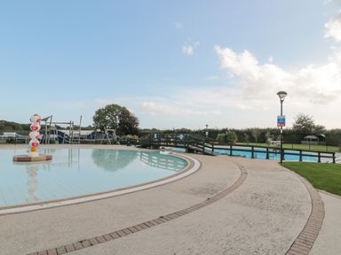 An outdoor swimming pool area with a small children's pool and a playground in the background at The Olive Lodge 227 Sycamore in New Milton