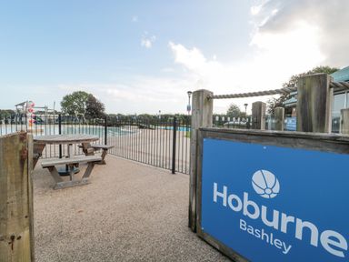 An outdoor pool area with a wooden picnic table and fenced swimming pools at Hoburne Bashley