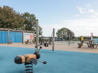 A playground with a spring rider shaped like an insect swings and picnic tables near a fenced pool area at The Olive Lodge 227 Sycamore in New Milton